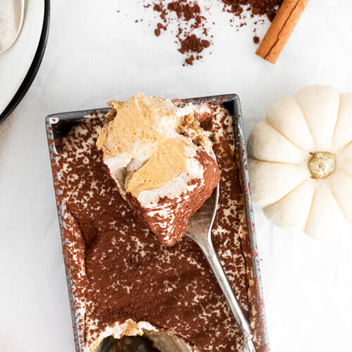 pumpkin tiramisu in a loaf pan with a spoon and a white pumpkin on the side.