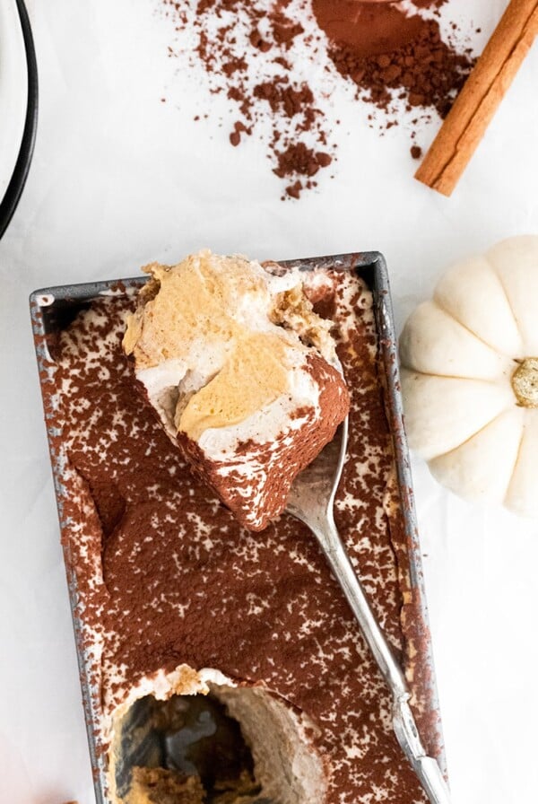 pumpkin tiramisu in a loaf pan with a spoon and a white pumpkin on the side.