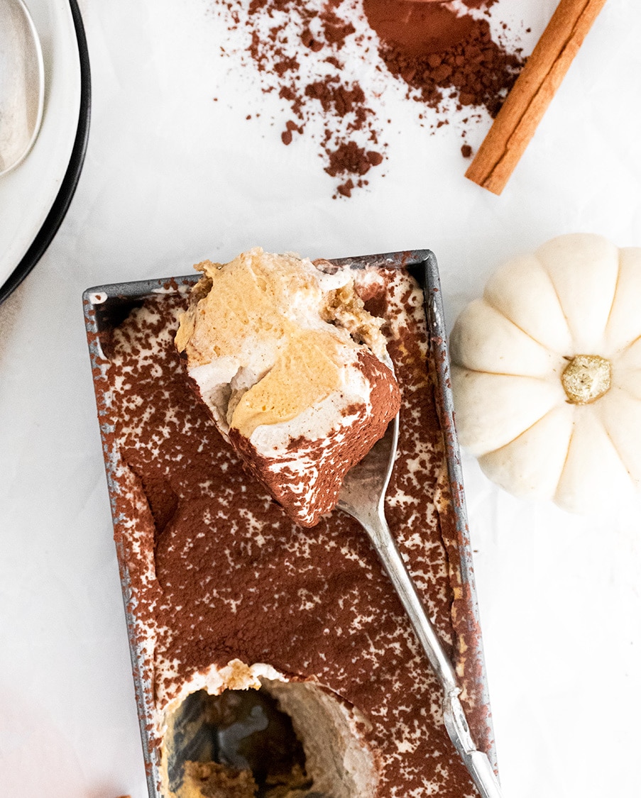 pumpkin tiramisu in a loaf pan with a spoon and a white pumpkin on the side. 