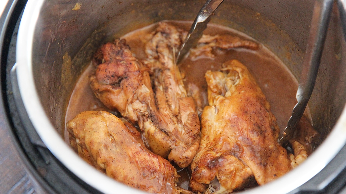 three smothered turkey wings in the instant pot with a pair of tongs.