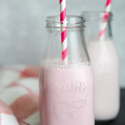 two milk jugs filled with strawberry milk and pink and white straws.
