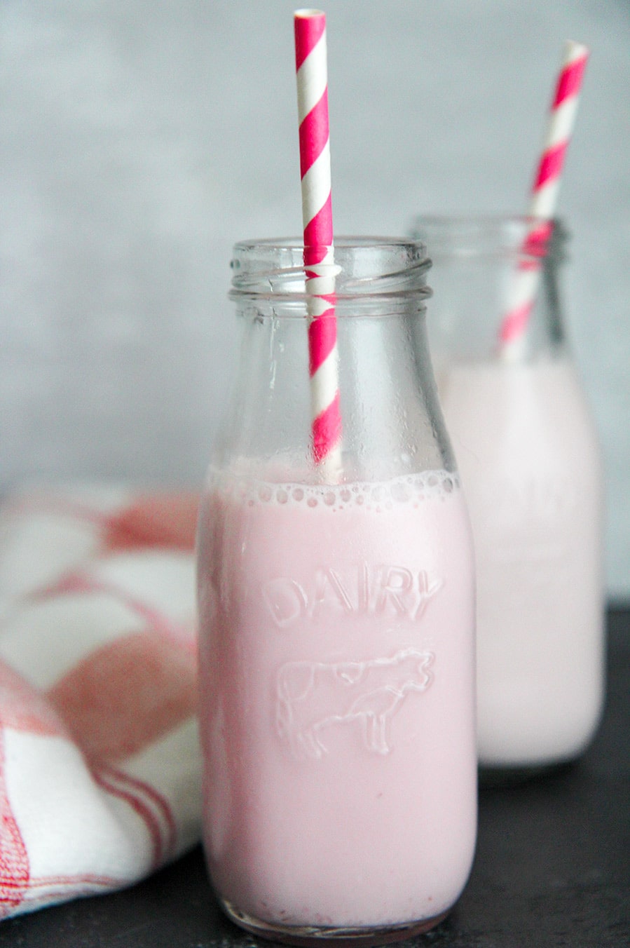 two milk jugs filled with strawberry milk and pink and white straws. 
