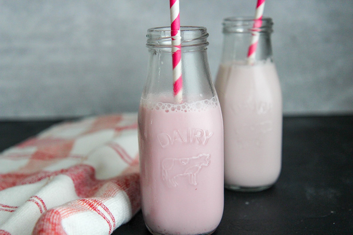 two milk jugs with strawberry milk, straws, and a red and white towel on the side. 