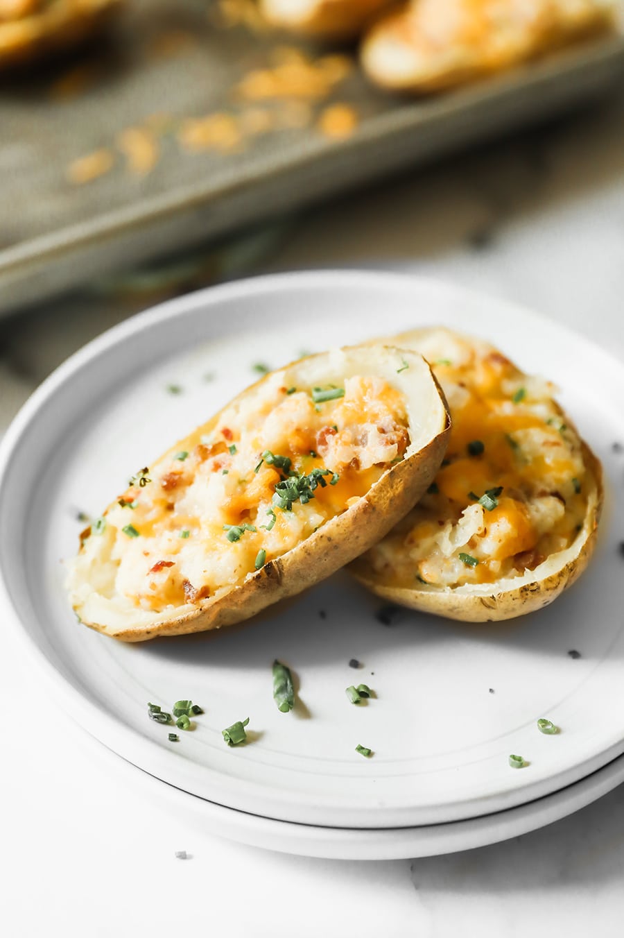 two twice baked potatoes on a white plate with green herbs on top. 