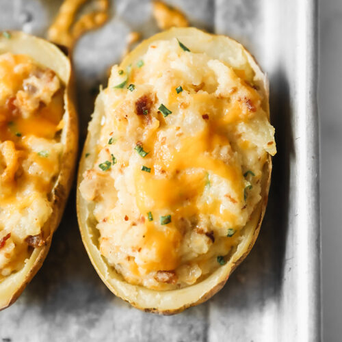twice baked potato with melted yellow cheese and green herbs on top.