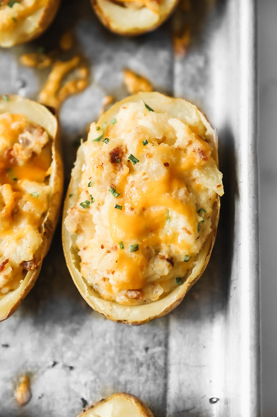 twice baked potato with melted yellow cheese and green herbs on top. 