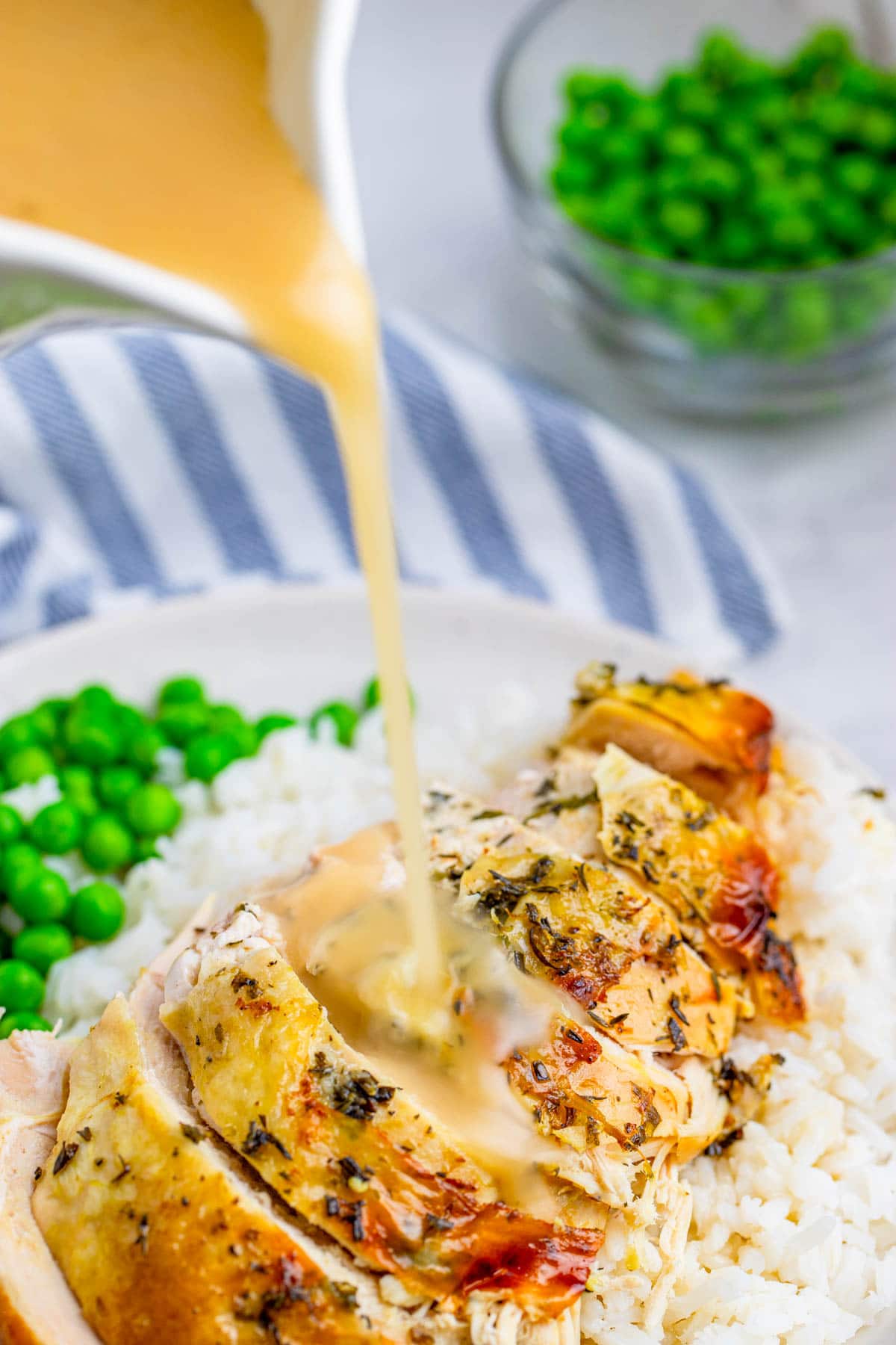 chicken, white rice, peas, and gravy on a white plate with a blue and white towel on the side. 