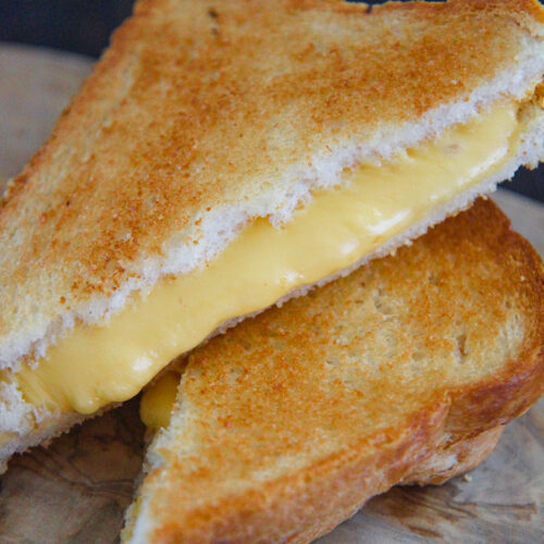 two grilled cheese sandwiches stacked on top of each other on a wooden board.