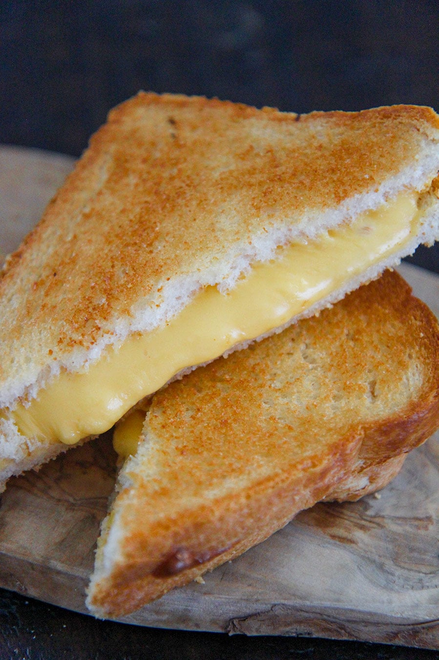 two grilled cheese sandwiches stacked on top of each other on a wooden board.