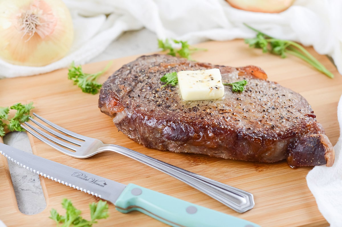 rib eye steak on a wooden board with a fork and knife. 
