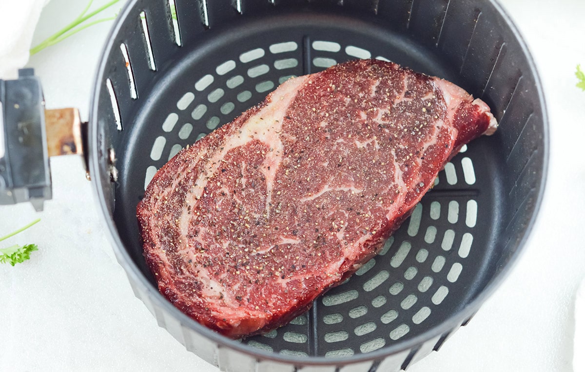 raw rib eye steak in the air fryer basket. 