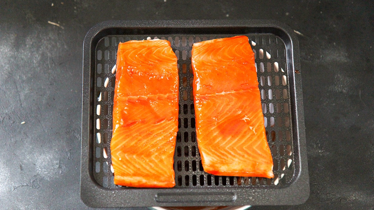 two raw salmon fillets on the air fryer basket. 