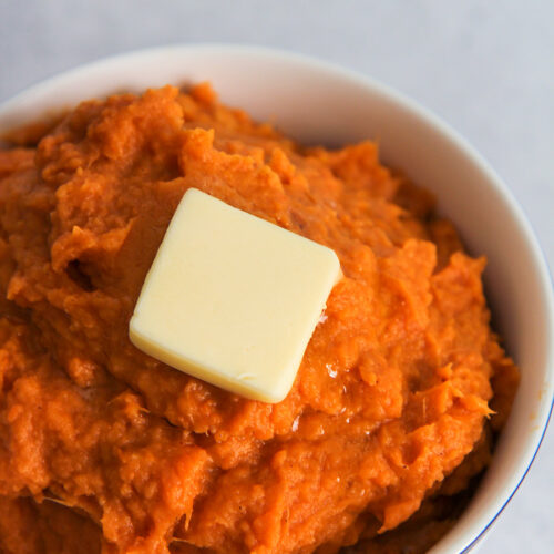 a small white bowl filled with mashed sweet potatoes and a slice of butter on top.
