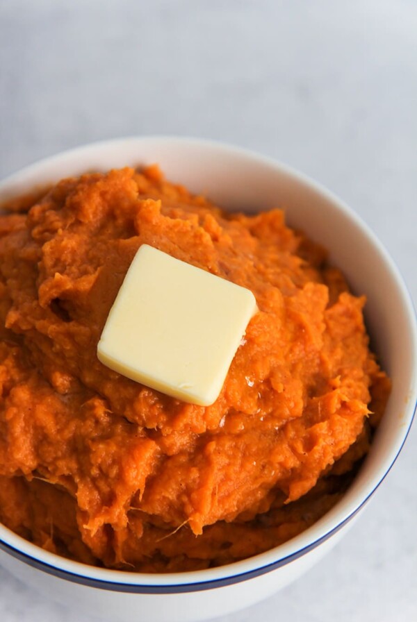 a small white bowl filled with mashed sweet potatoes and a slice of butter on top.