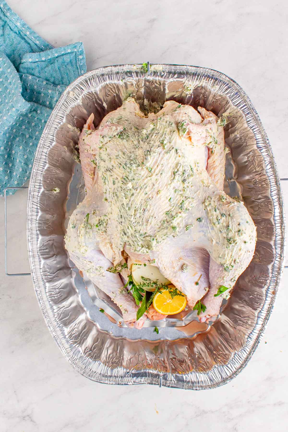 raw turkey smothered with softened butter and herbs inside a baking dish. 