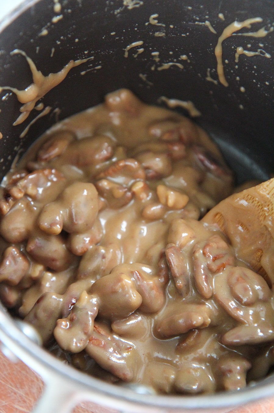 pecan mixture in a black saucepan with a wooden spoon.