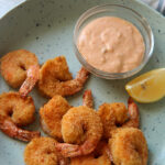 air fried shrimp on a blue plate with a lemon wedge and sauce in a bowl.
