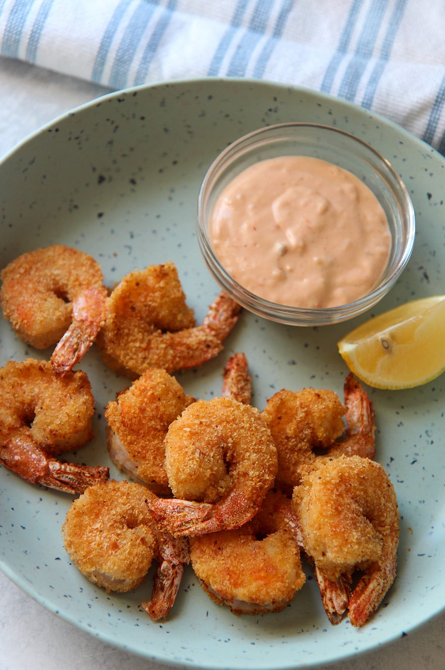 air fried shrimp on a blue plate with a lemon wedge and sauce in a bowl.