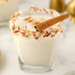 coquito in a short glass with toasted coconut on the rim and a cinnamon stick on top.