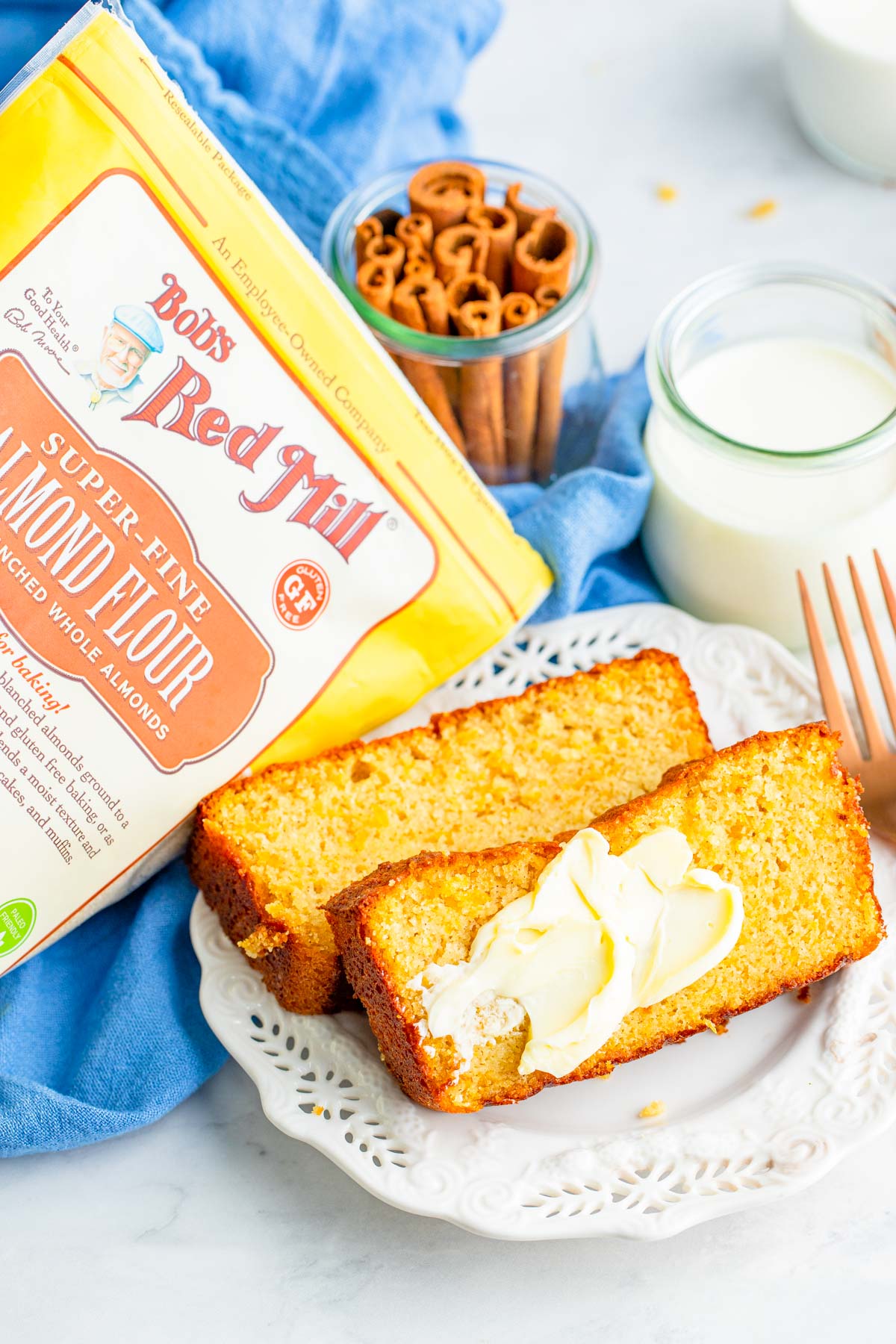 two slices of sweet potato bread with butter, a fork on the side, a glass of milk, and a package of bobs red mill almond flour. 