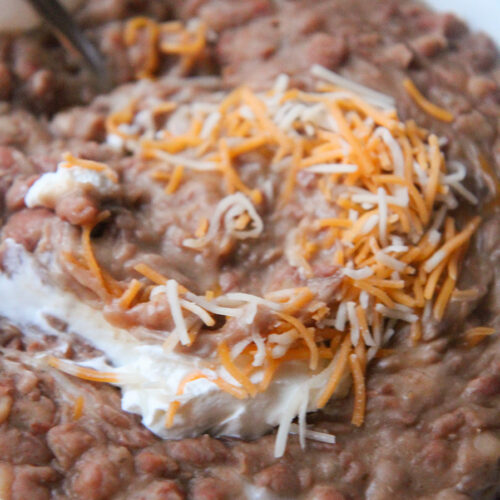 refried beans with sour cream, a spoon, and cheese in a small bowl up close.