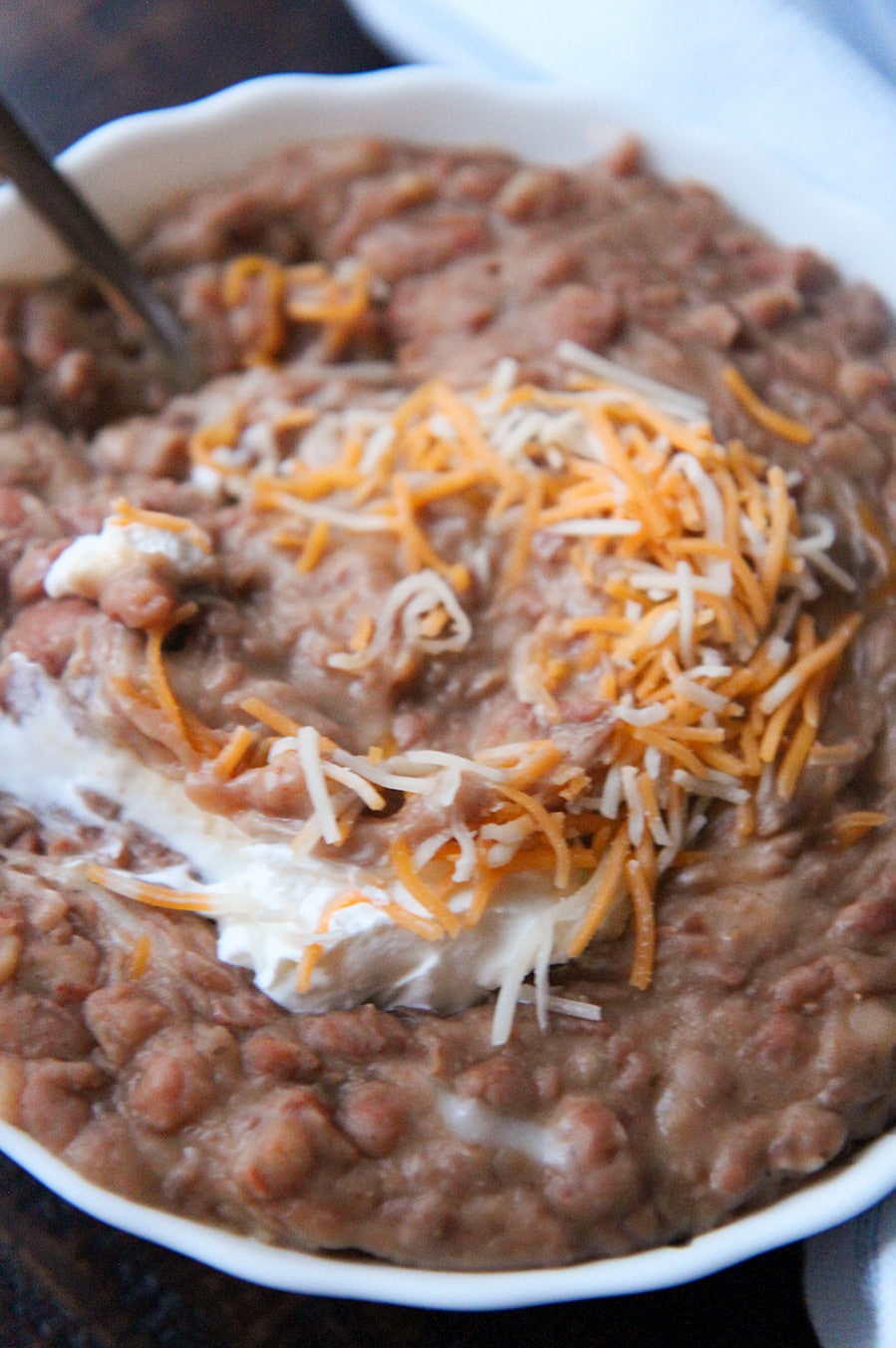 refried beans with sour cream, a spoon, and cheese in a small bowl up close. 