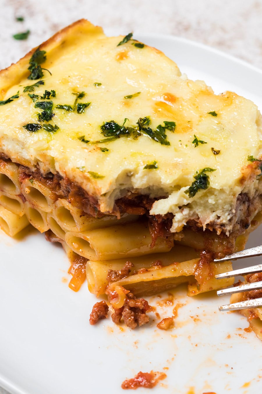 a slice of Greek lasagna on a white plate with a fork on the side. 