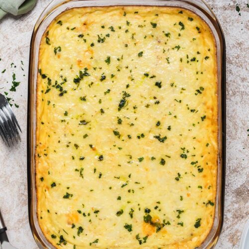 Baked pastitsio in a glass baking dish with chopped parsley on top.