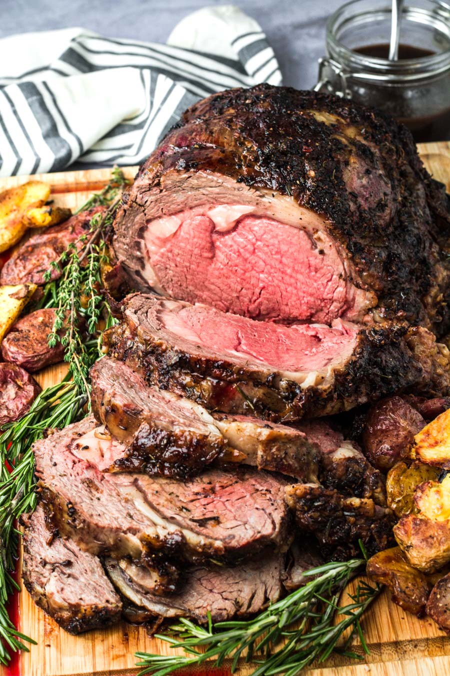 sliced prime rib medium rare on a wooden board with fresh rosemary and thyme.