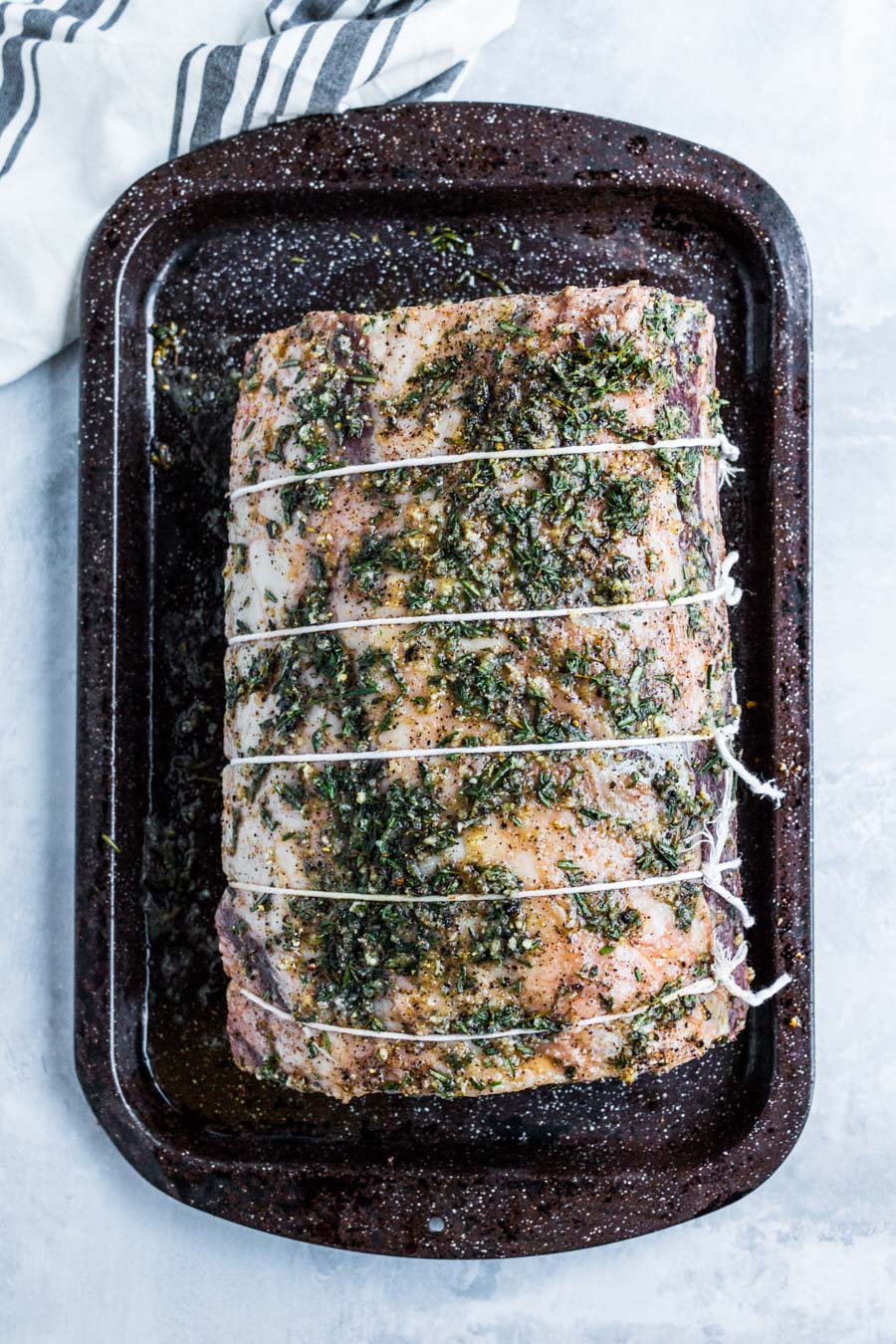 an entire raw prime rib tied with kitchen twine on a baking sheet.