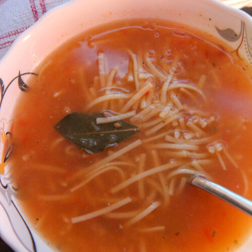 a bowl of sopa de fideo with a spoon and a red and white towel on the side.