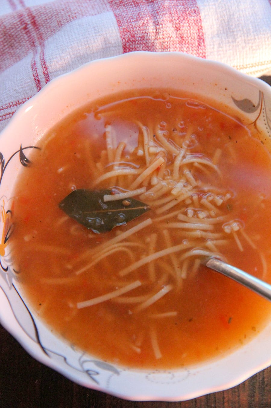 a bowl of sopa de fideo with a spoon and a red and white towel on the side.