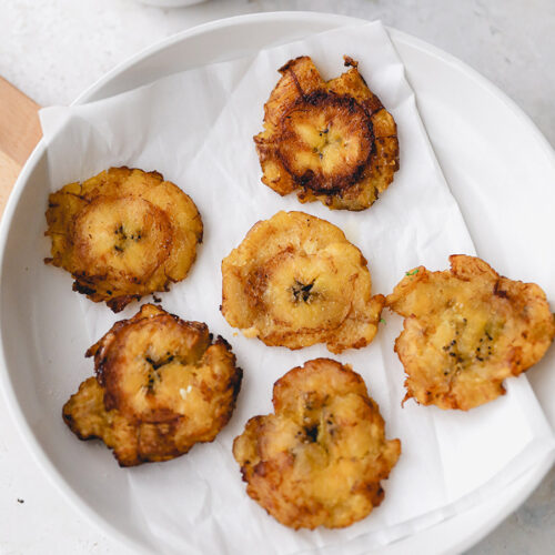 6 tostones on a white plate with a side of garlic butter sauce.