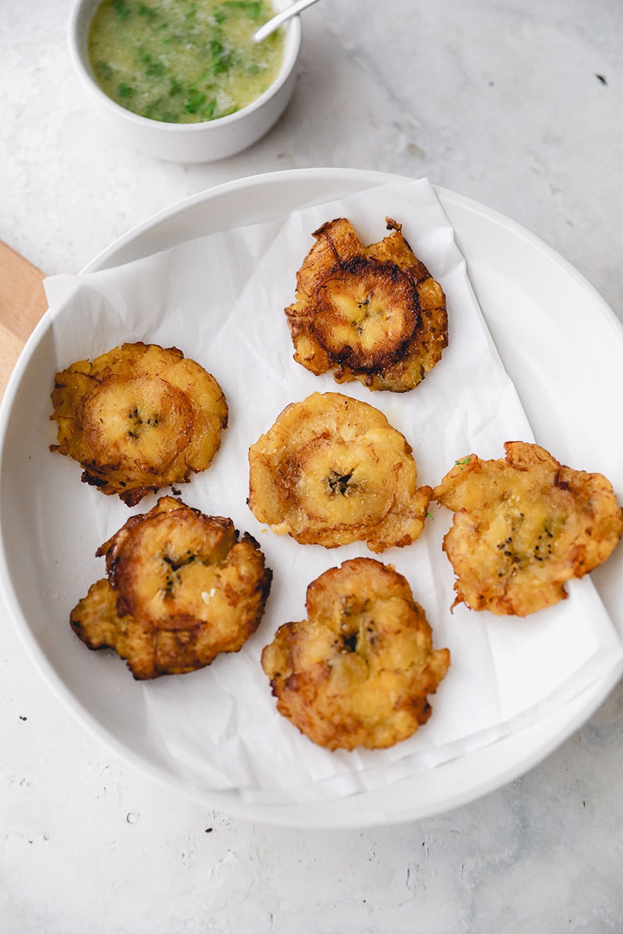 6 tostones on a white plate with a side of garlic butter sauce. 