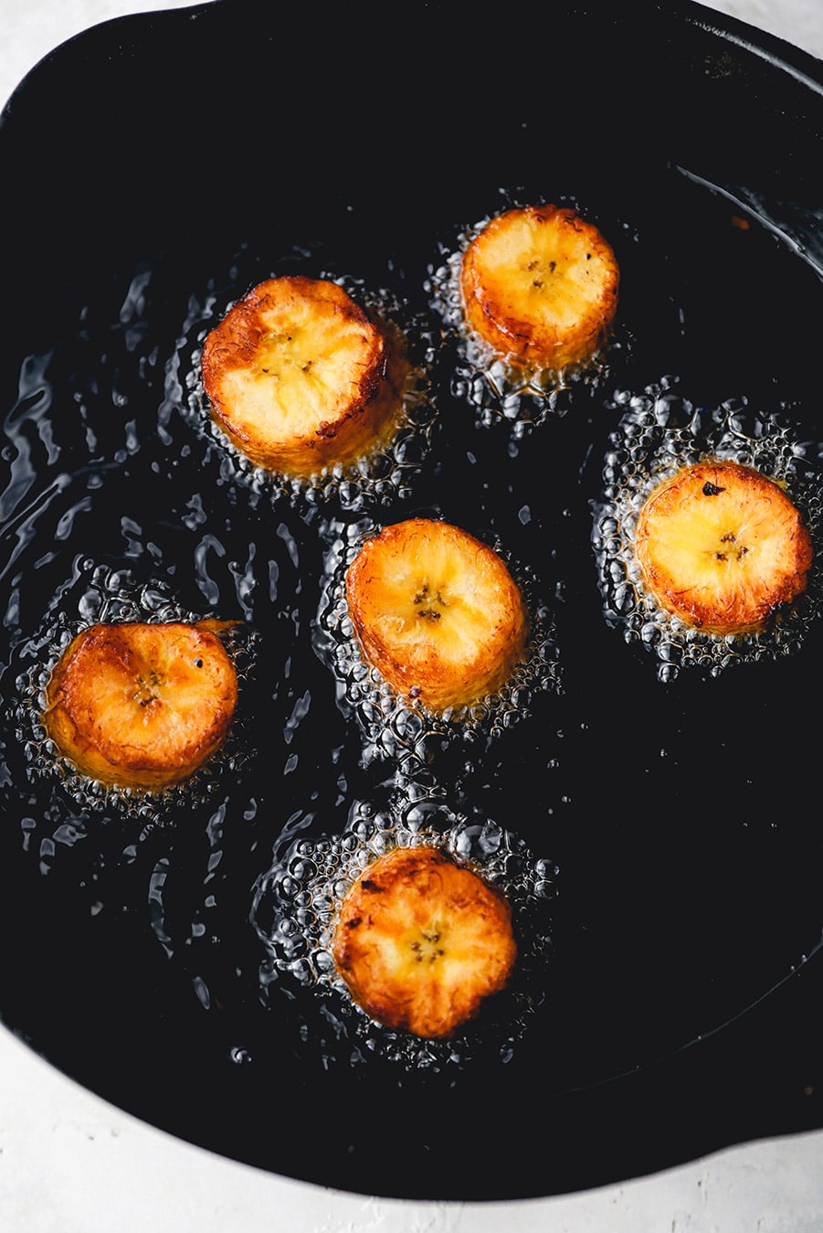 6 plantains frying in a cast iron skillet. 