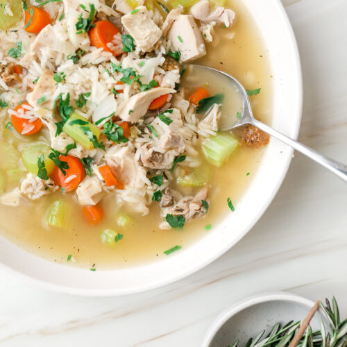 leftover turkey and rice soup in a white bowl with fresh rosemary on the side.