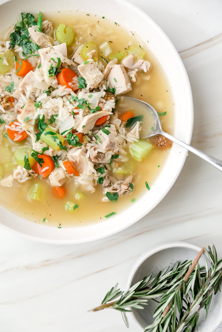leftover turkey and rice soup in a white bowl with fresh rosemary on the side. 