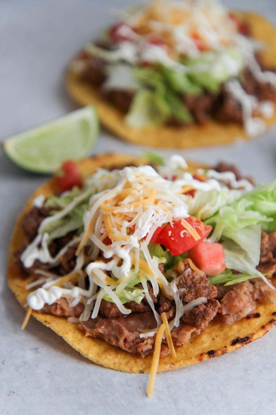 two beef tostadas with refried beans, lettuce, tomatoes, cheese, sour cream, and limes on the side. 