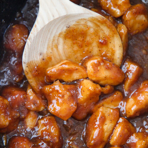 orange chicken in the slow cooker with a wooden spoon.