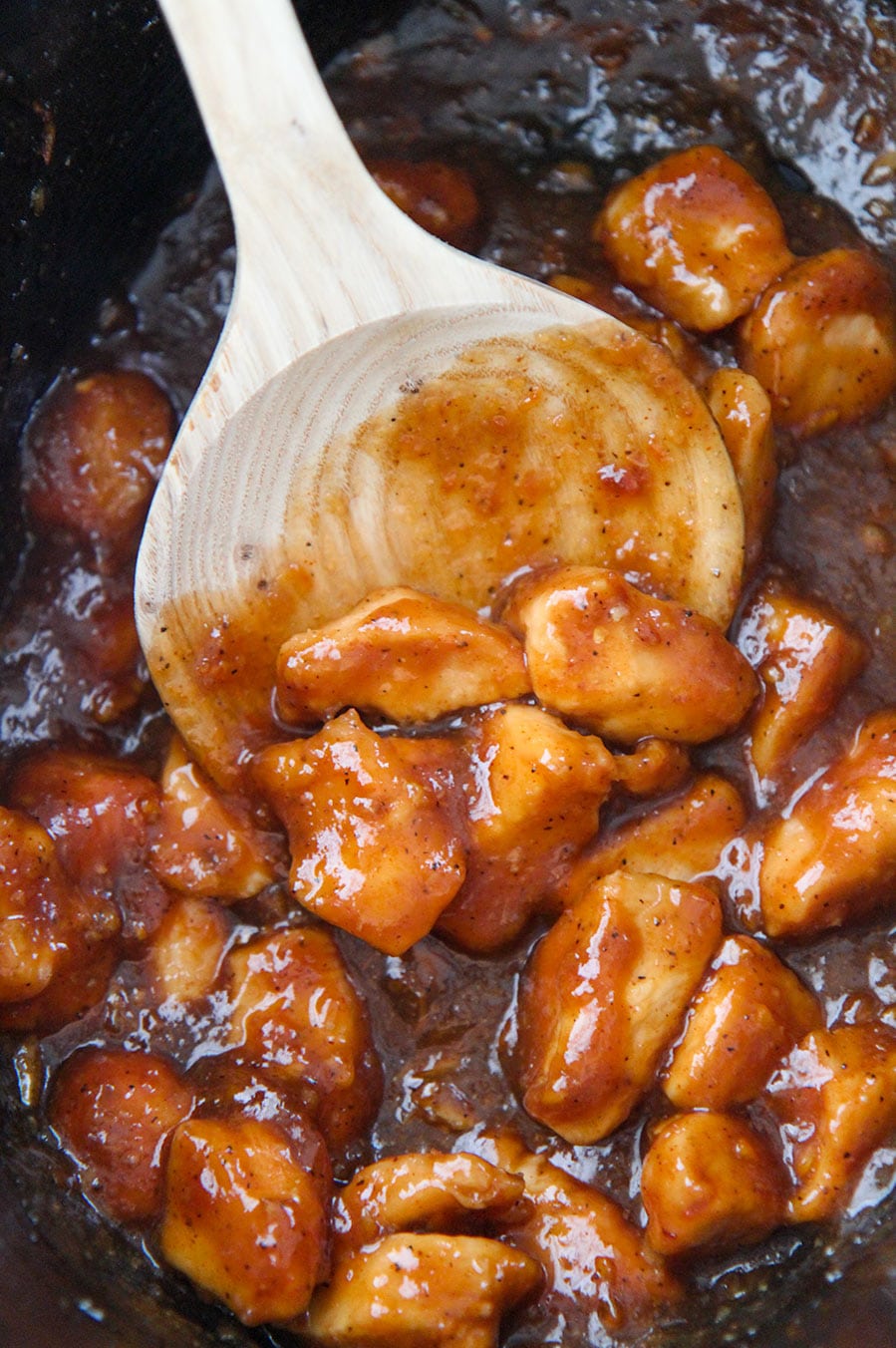 orange chicken in the slow cooker with a wooden spoon.