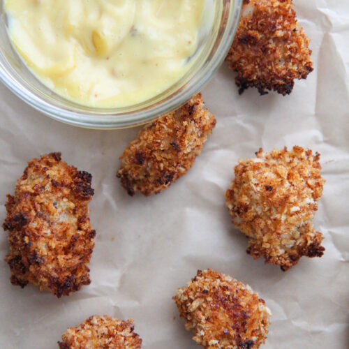 baked spicy popcorn chicken bites on brown parchment paper with a side of honey mustard.