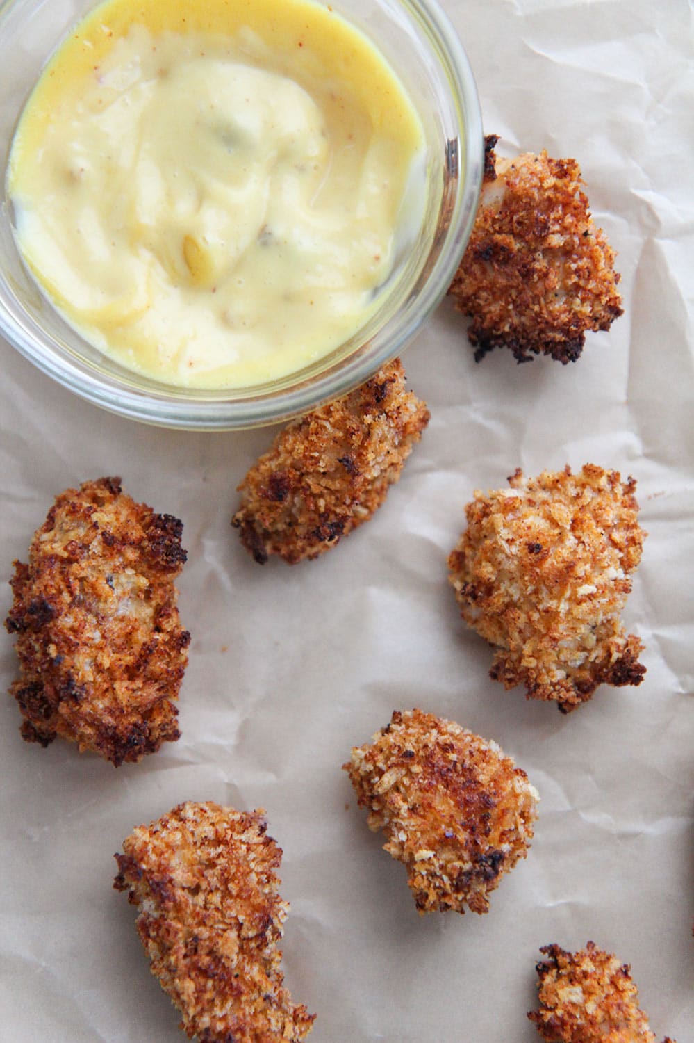 baked spicy popcorn chicken bites on brown parchment paper with a side of honey mustard.