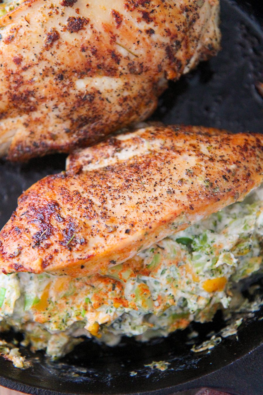 two broccoli cheese stuffed chicken breasts in a cast iron skillet.