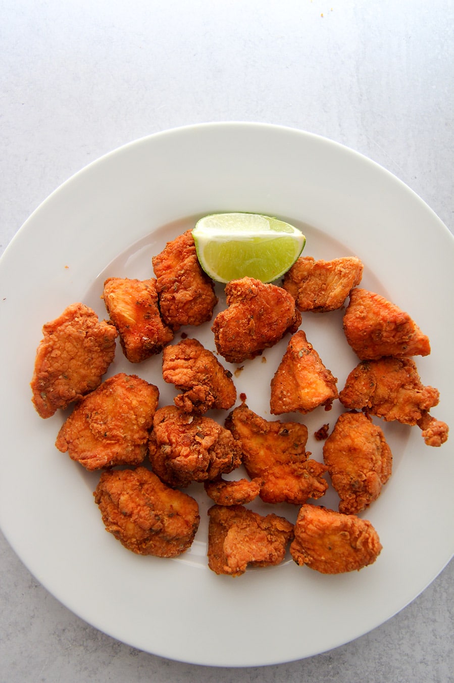 chicharron de pollo aka chicken bites on a white plate with a lime wedge.