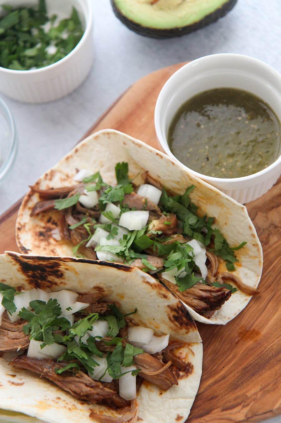 two instant pot pork carnitas tacos on a wooden board with green sauce on the side. 