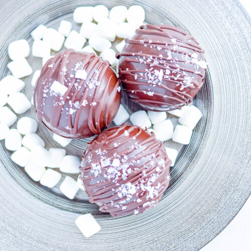 three hot chocolate bombs on a plate with mini marshmallows.