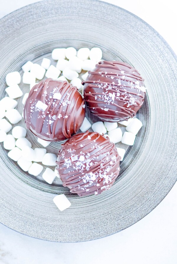 three hot chocolate bombs on a plate with mini marshmallows.