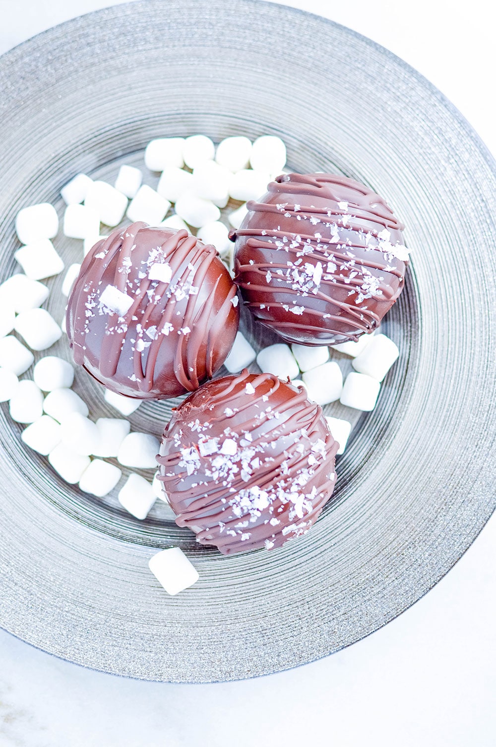 three hot chocolate bombs on a plate with mini marshmallows.