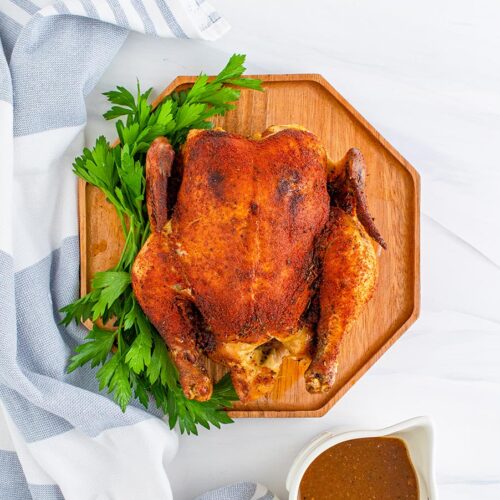 cooked whole chicken on a cutting board with gravy on the side.