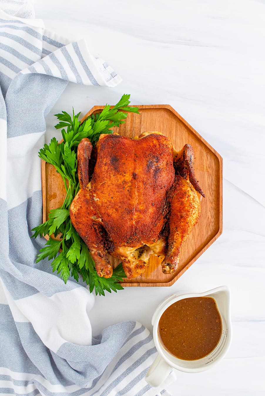 cooked whole chicken on a cutting board with gravy on the side. 